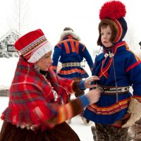 На иллюстрации из цитируемой здесь официальной публикации «Саамы в Швеции», изданной «Шведским институтом» в 2014 году: Шведские саамы в шведской же части Лапландии в национальных костюмах. Напомним что Лапландия - это традиционная арктическая область расселения саамов, части этой области ныне поделены между Норвегией, Швецией, Финляндией и Россией. Отметим, что название «Лапландия», как и свое прошлое наименование «лопари», саамы не слишком жалуют (о причинах см. в нашем обзоре). Саамы называют Лапландию Сапми (Sápmi, «земля саамов»). Что же касается национального костюма, то как напоминает цитируемая, среди прочего, ниже официальная публикация «Саамы в Швеции», изданная в 2014 г. «Шведским институтом»: «Национальный костюм саамов – гакти, гакты или кафты, который они надевают по особым случаям. Традиционный костюм различается для мужчин и женщин, а узоры зависят от географического региона. Детская гакти с аксессуарами – это точная копия взрослой гакти, только меньшего размера… (При этом) можно определить, из какого региона родом тот или иной саам по его гакти…».